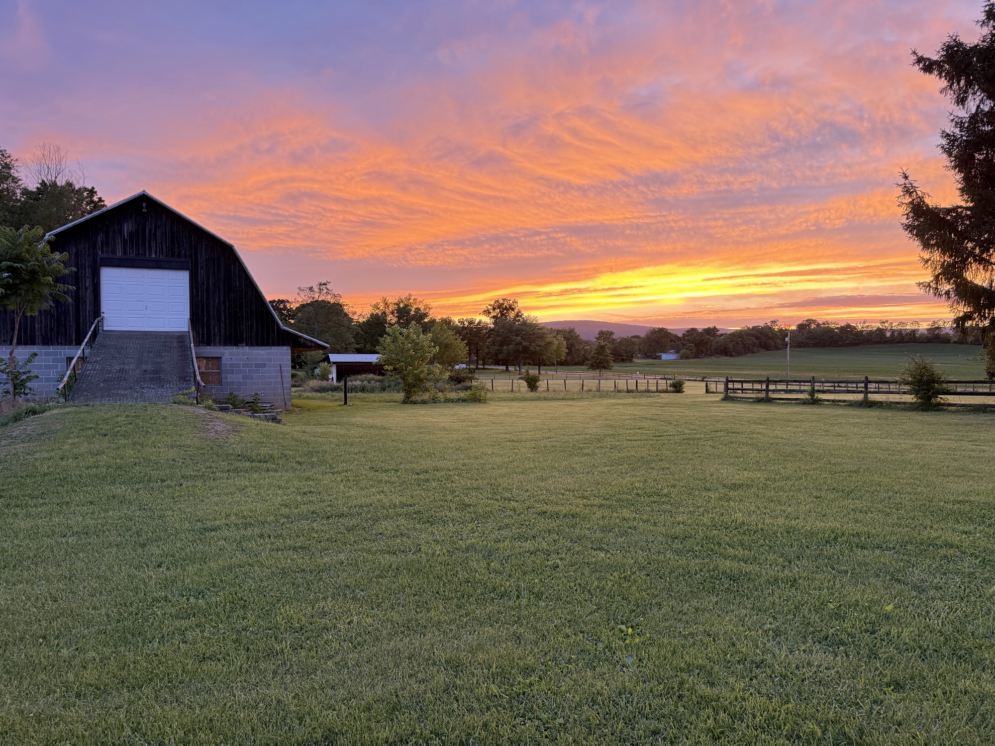 The rust-red barn at Art Farm under a sunset sky
